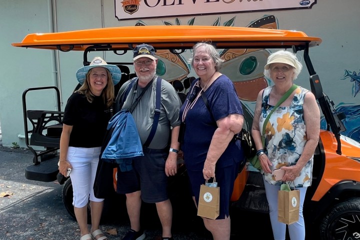 Four people smiling in front of an orange golf cart at Olive Morada.