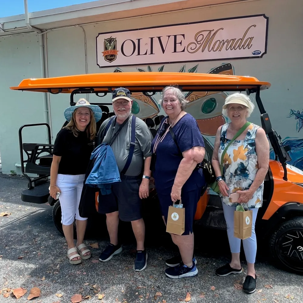 Four people smiling in front of an orange golf cart at Olive Morada.