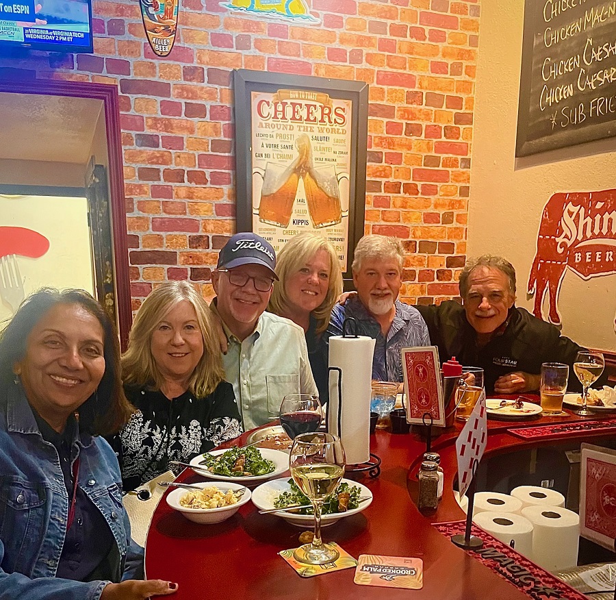 Group of six people smiling at a restaurant table with food and drinks.