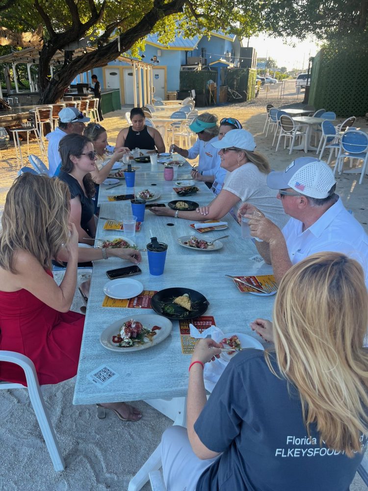 Group of people dining outdoors at a long table under a tree.