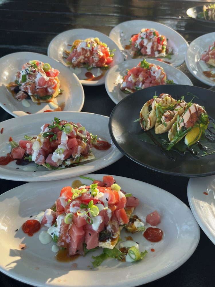 Plates of diced raw fish and garnishes on white dishes, with tacos on a black plate.