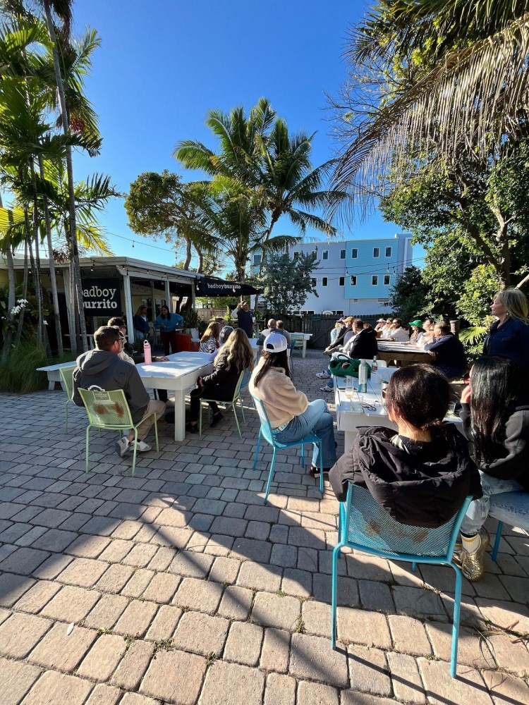 People seated outdoors at tables near 'badboy burrito' under palm trees, enjoying a sunny day.