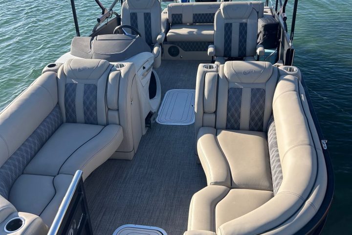 Pontoon boat with beige seats and American flag, floating on calm water.