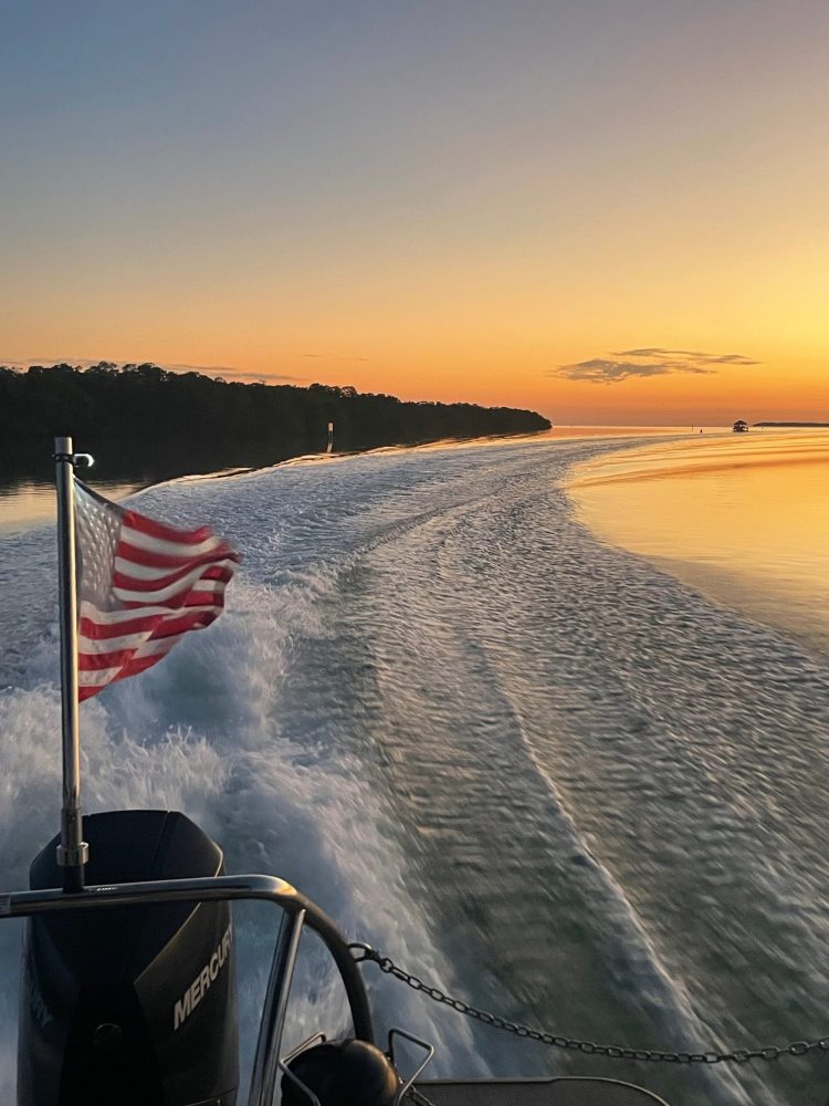 Poppa Toon Boat with American flag on water at sunset in Islamorada, leaving a wake behind.