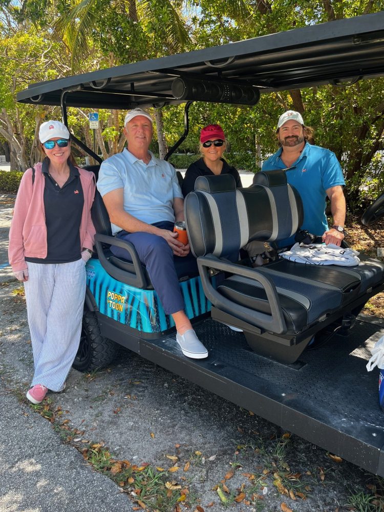 Four people smiling, sitting on a golf cart under trees on an islamorada luxury golf cart food otur