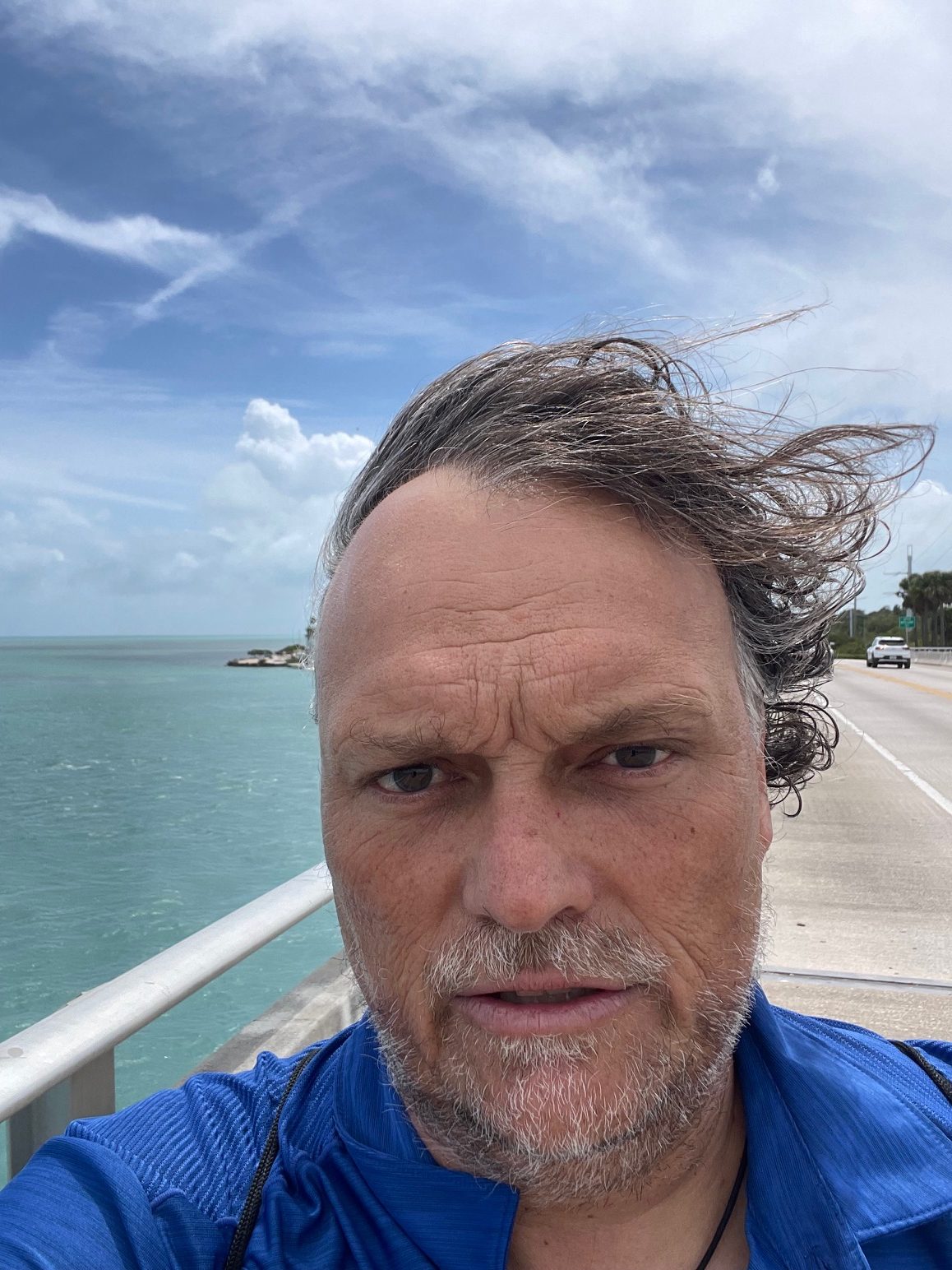 Man in blue shirt walking in the wind next to the turquoise water of Islamorada, Florida Keys.
