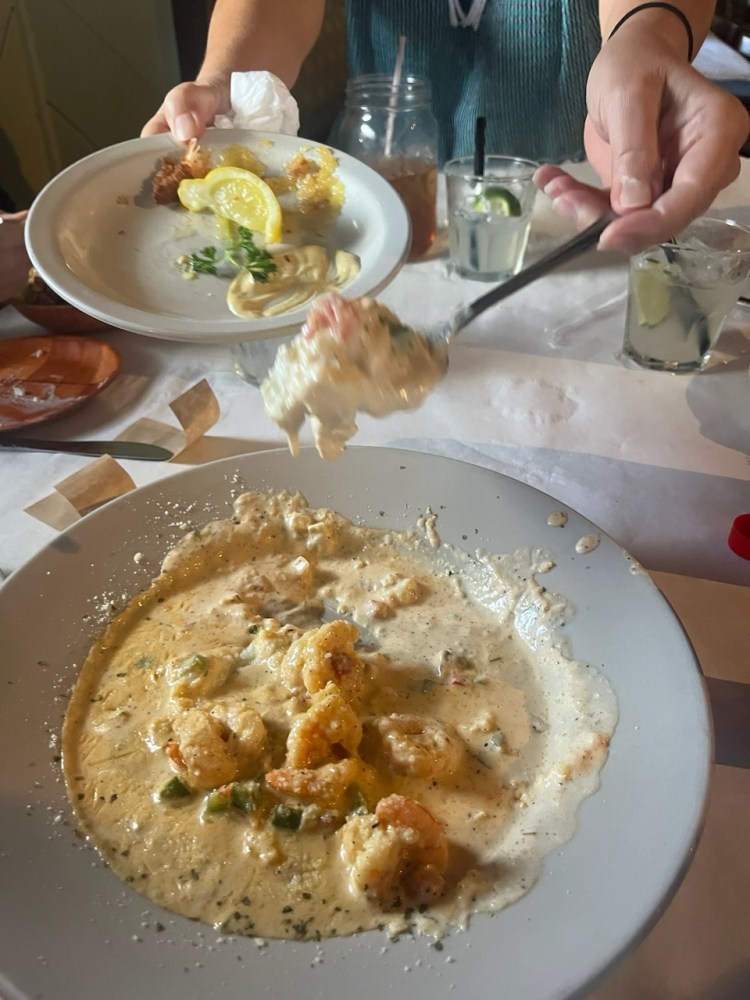 Hands serving creamy shrimp and grits dish from large bowl onto a small plate at the shrimp shack in islamorada.